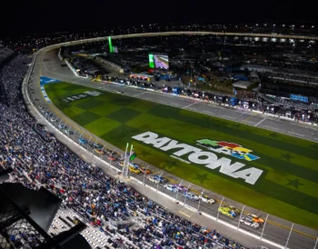 Nighttime view of Daytona International Speedway with race cars on track.